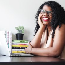 Eternity Martis sitting at a desk with an open laptop, a pile of books and a cactus.