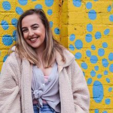 Valerie Dittrich against a wall painted yellow and blue.